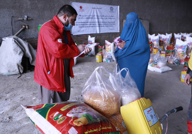 AARスタッフと受け取りの手続きをする女性。近くには食料の支援物資がある