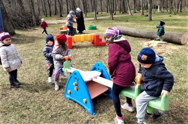 屋外で、シーソーなどの遊具で子どもたち7,8人が遊んでいる
