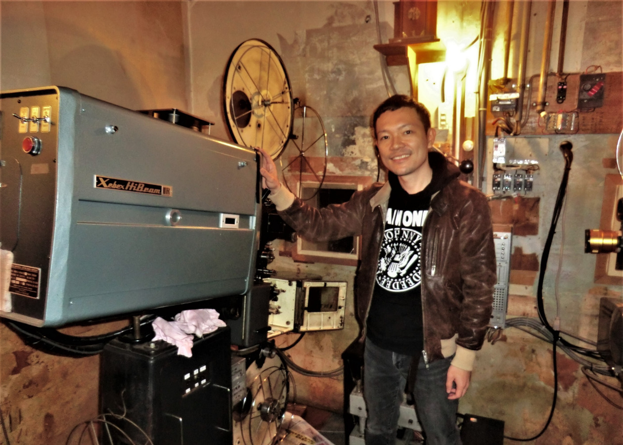 上野さんが自身の高さほどもある大きな映写機の横で微笑む