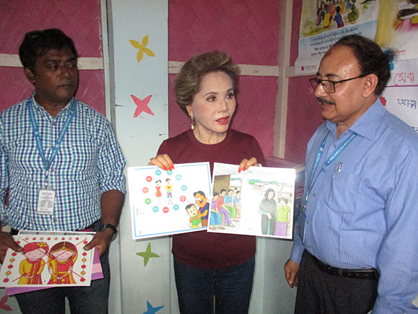 子どもや人身売買などのイラストが描かれた2枚の紙を夫人が手にしている。左右にいる現地NGOの男性が絵の内容などを説明している
