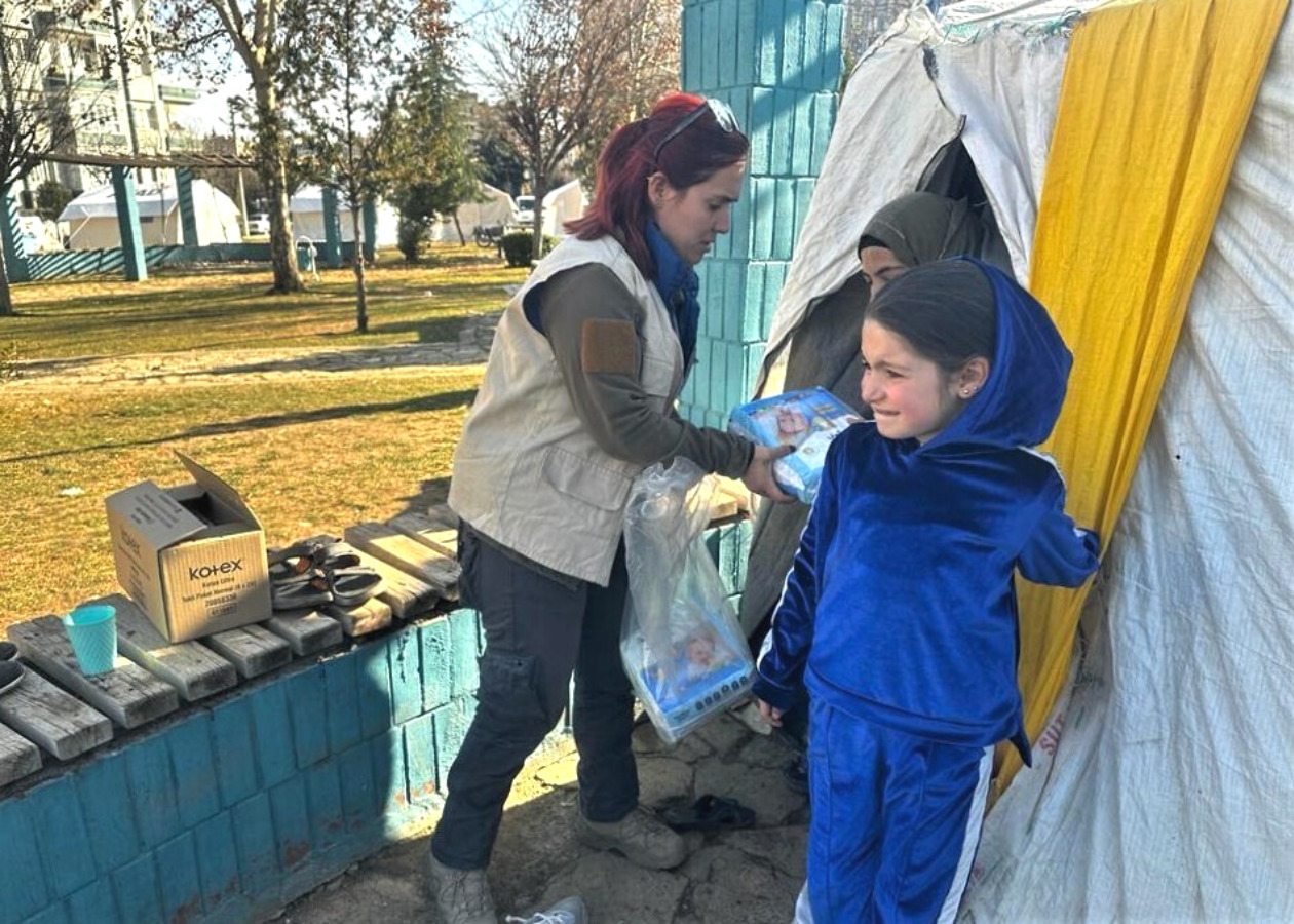 テントのそばには子どもが立っている。AAR職員はテントの中にいる被災者に物資を渡している
