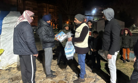 寒い外に何人ものトルコ地震被災者が立っている。その一人に支援物資を手渡すAARスタッフ