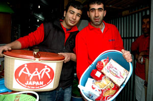 トルコ人の男性二人が食糧がはいった入れ物を持っている