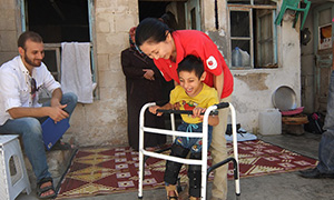 歩行器をつかんで歩く少年を支えるAARスタッフの写真