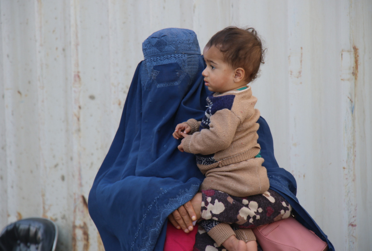 布で顔を覆った母親が子どもを抱いている写真