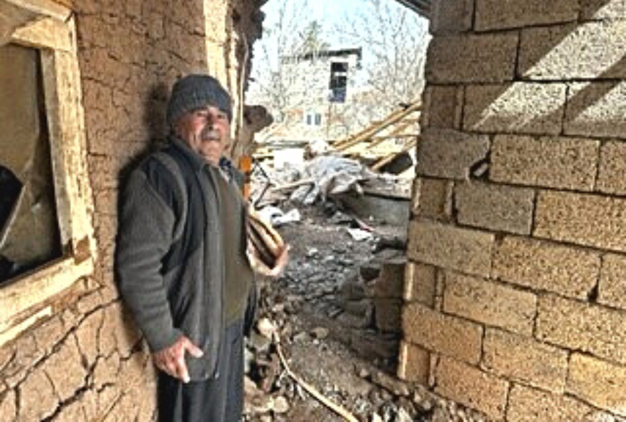 倒壊した自宅の前に立っているメフメットさんの写真
