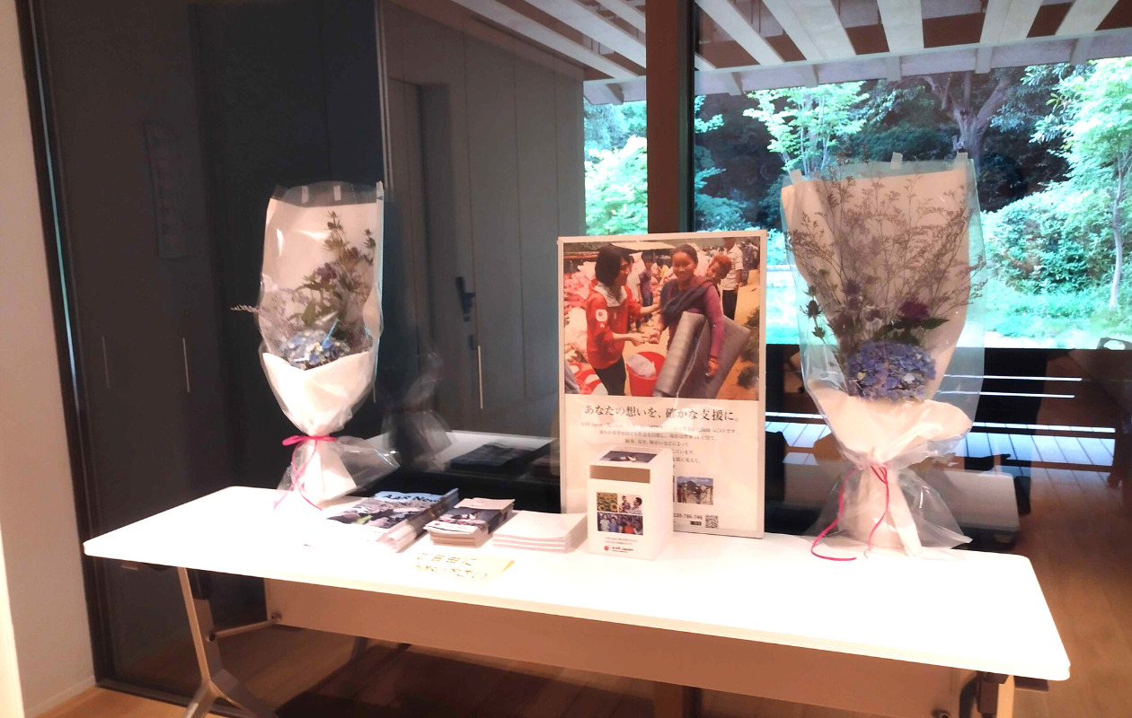 テーブルの設置されたAARのポスター、募金箱、パンフレット、花束
