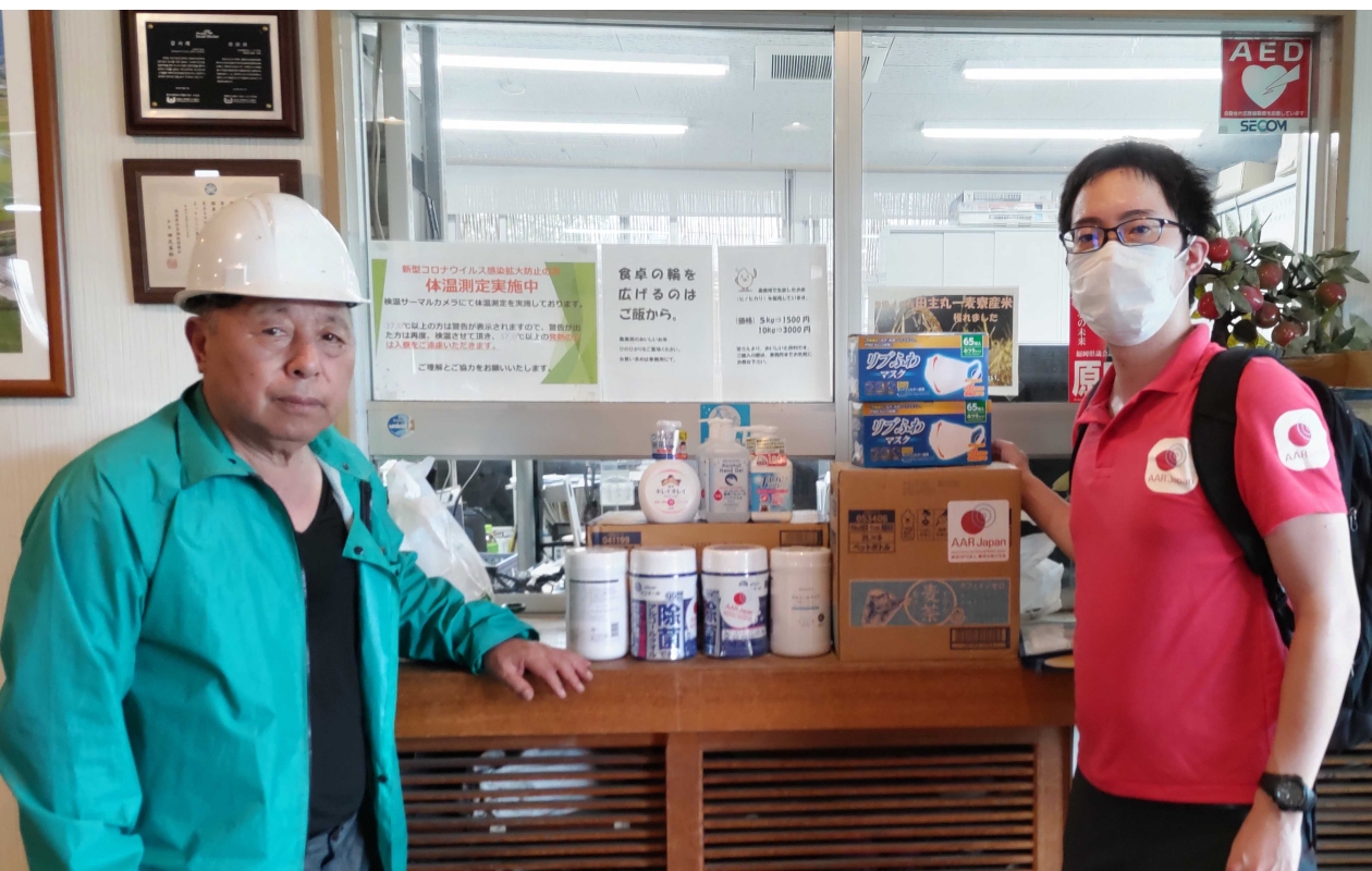 ヘルメットを着用した理事長の郷原和彦さんとAARの生田目が、緊急支援物資の前に立っています