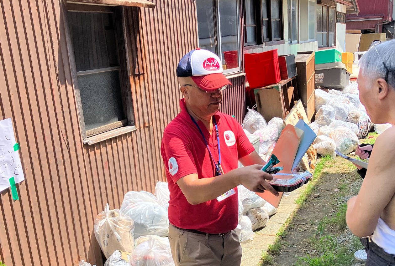 災害ゴミが積まれた住宅街でお弁当を届けるAAR職員