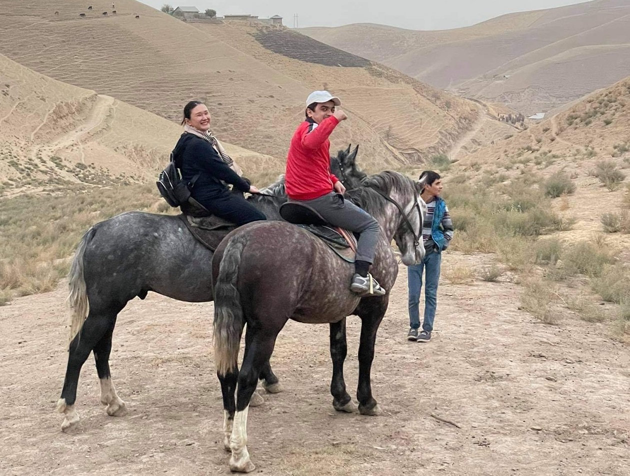 タジキスタンの高原で、笑顔で馬に乗る東マリ子職員。