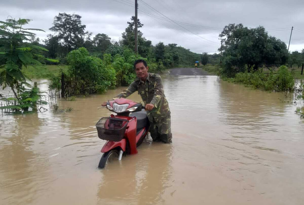 膝まで浸水した地域でバイクを押す男性の写真