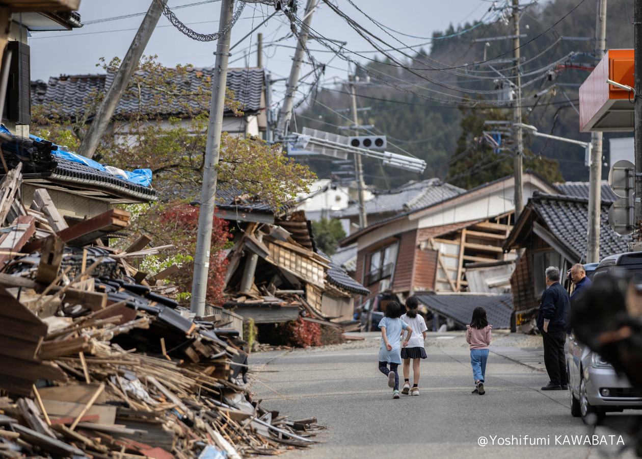 家屋が倒壊した町を３人の子どもが歩いている