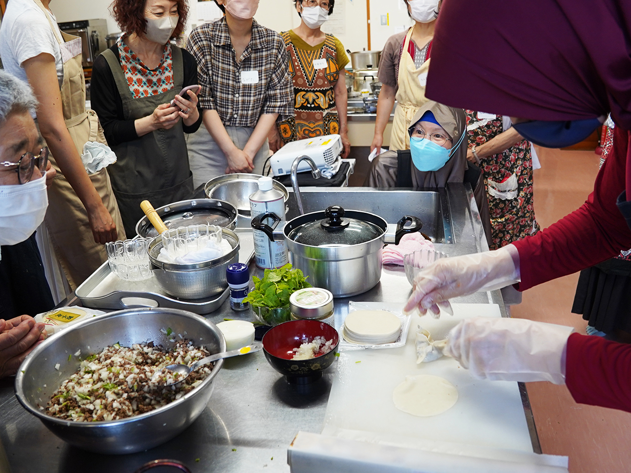 女性が調理する調理台を、参加者が囲んでいる