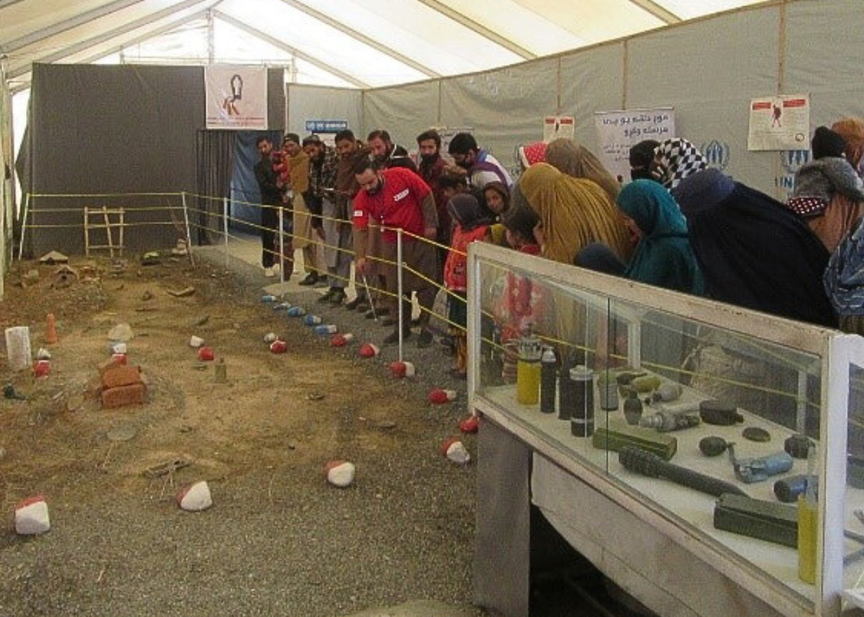 テントの中に土が敷かれ地雷原を再現。それを説明するAAR職員と参加者の助成たち