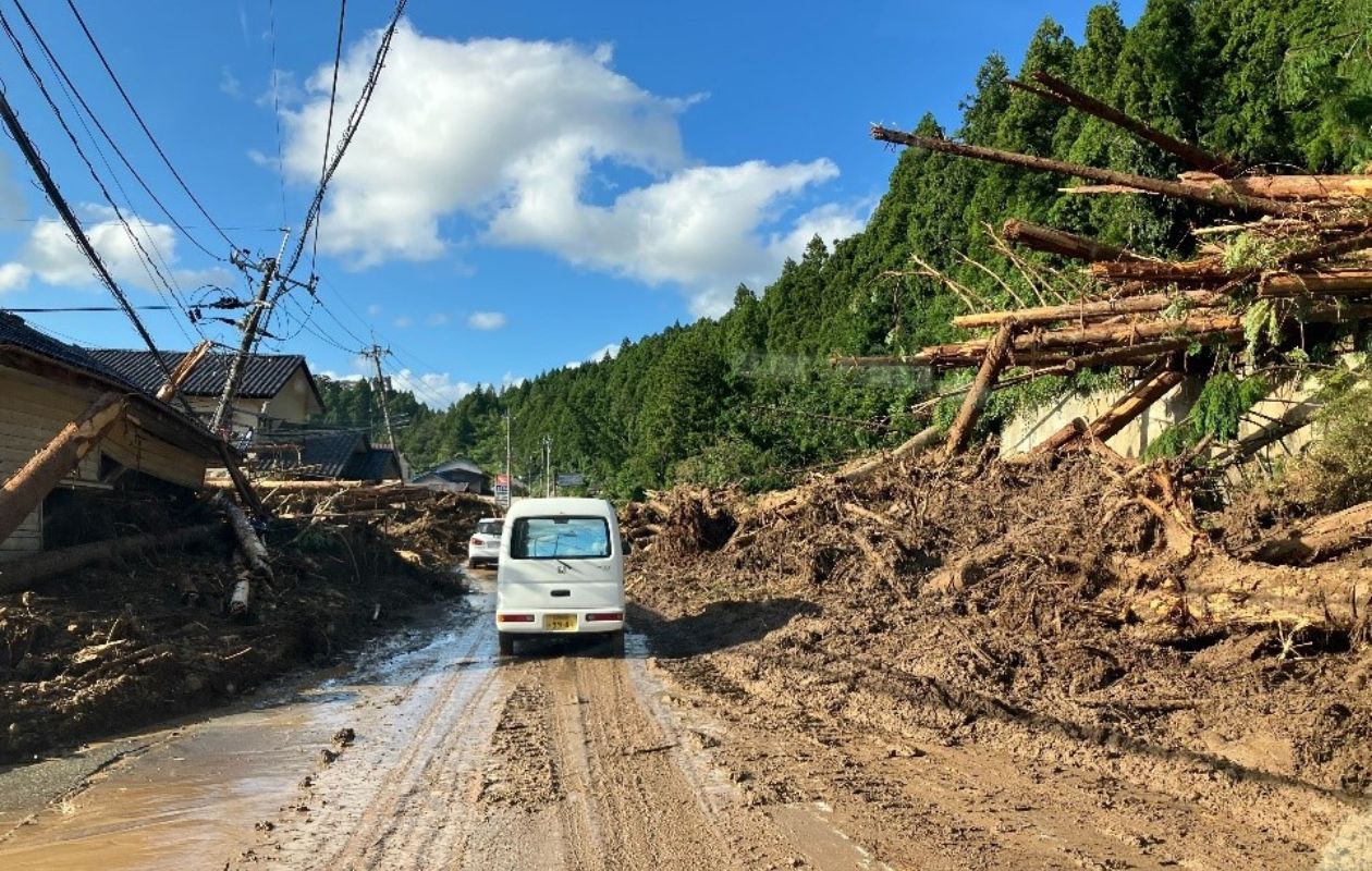 流木や土砂のなかを進む白い車