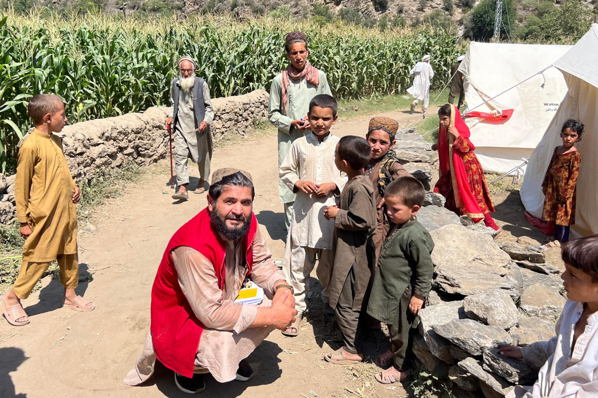 テントの前に集まる子どもたちの話を聞くAARカブール事務所の職員