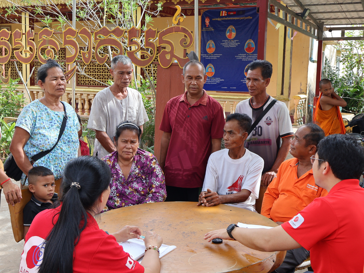 椅子に座って話す女性を人々が囲んで話を聞いている