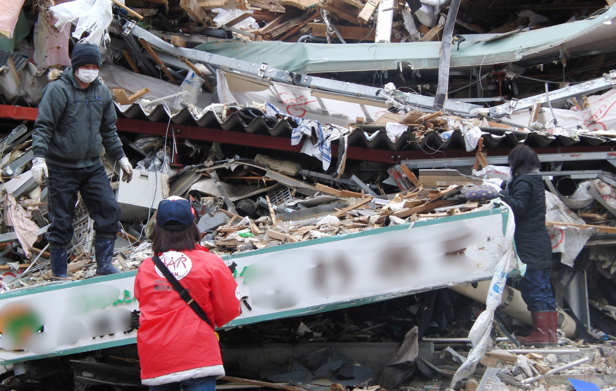 がれきの前で、被災者から話を聞く、野際の後ろ姿