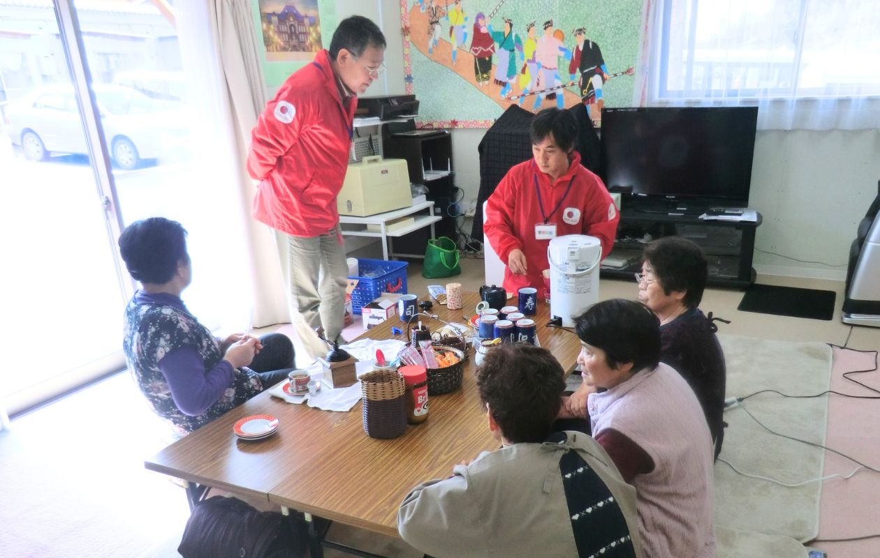 仮設住宅の集会場で、座卓を囲って座る女性たちとAARのスタッフ。