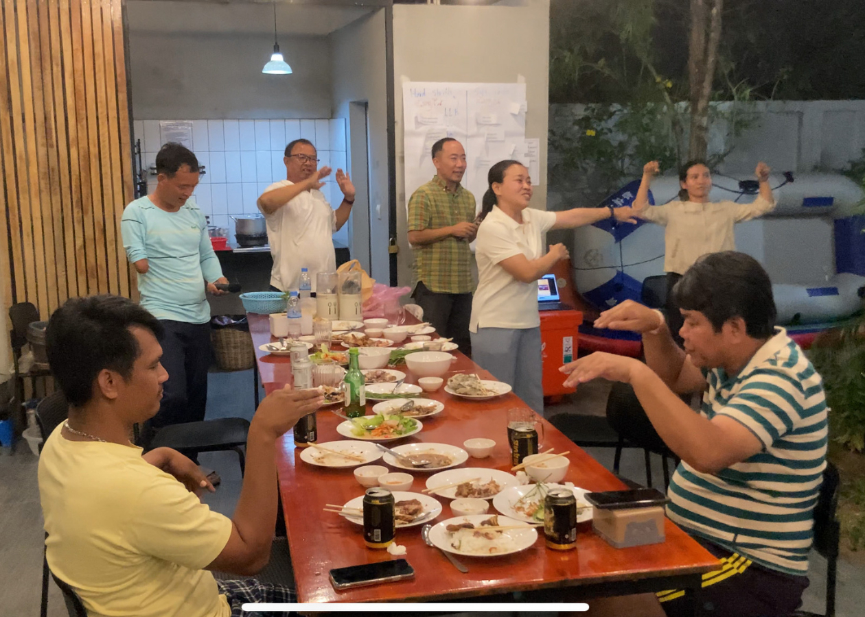 長テーブルに食事が置かれている。男女がカラオケをしながら楽しそうに踊っている